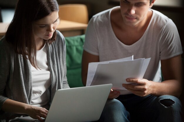 Serious millennial couple paying bills online on laptop at home