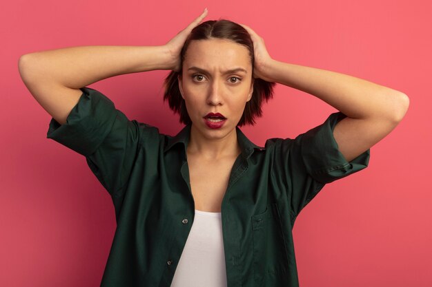 Serious pretty woman holds head isolated on pink wall