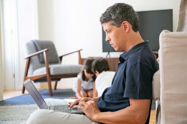 Serious professional working at home, sitting on floor and using laptop