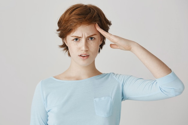 Serious redhead girl posing against the white wall