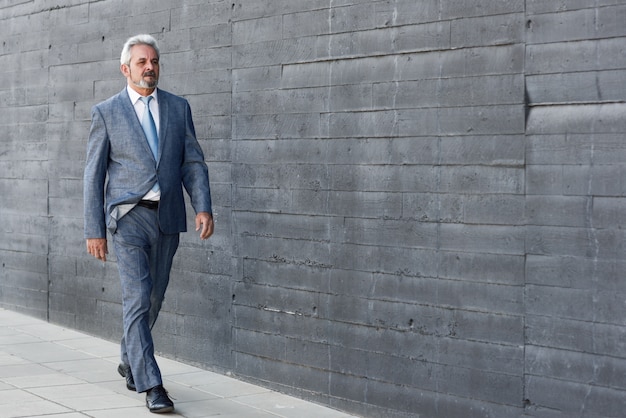 Free Photo serious senior businessman walking outside of modern office building.