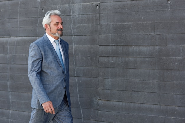 Serious senior businessman walking outside of modern office building.