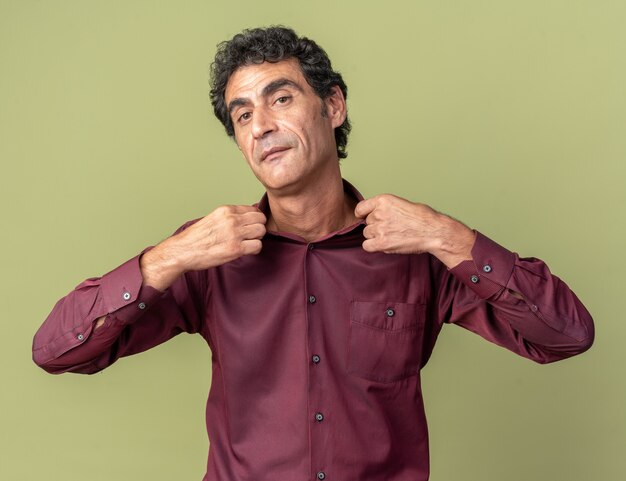 Serious senior man in purple shirt looking at camera with confident expression fixing his collar 