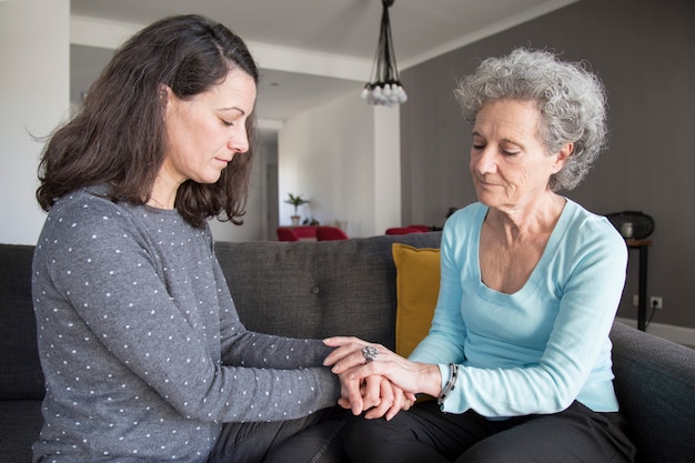 Free photo serious senior woman and her daughter holding hands