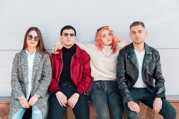 Serious and stylish teenagers sitting on bench on street