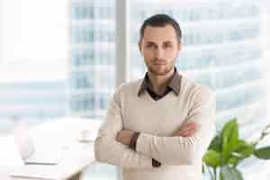 Free photo serious successful young businessman standing in office looking at camera