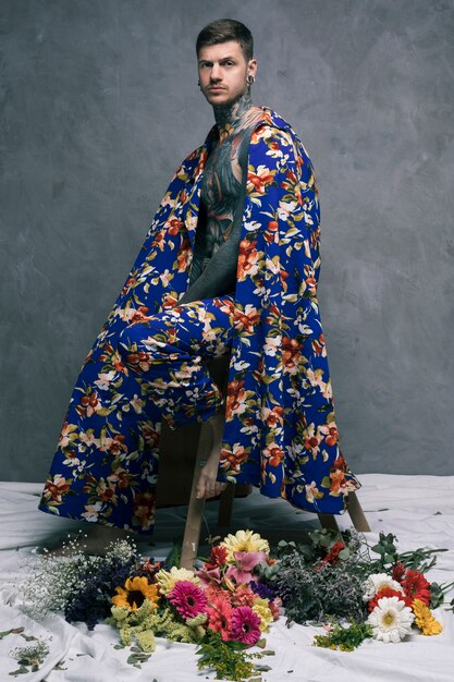 Serious tattooed young man in floral drape looking at camera