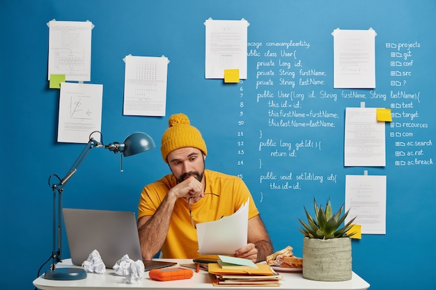 Free photo serious unshaven male manager in yellow outfit looks through financial documentation