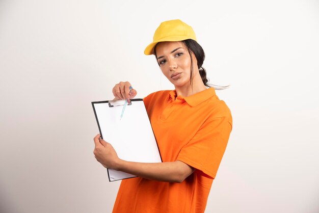 Serious woman courier showing clipboard on white wall.