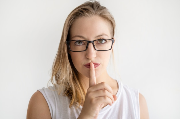 Serious woman making silence gesture and looking at camera