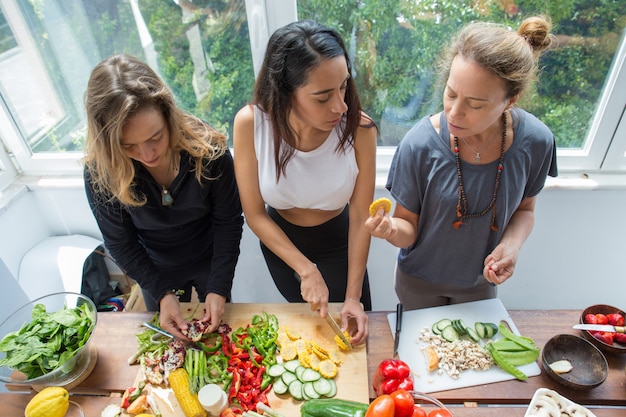 Free photo serious women chatting and cutting vegetables in kitchen