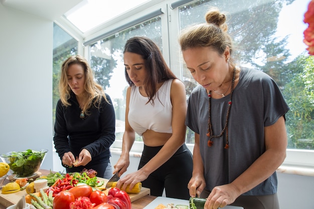 Serious women cooking and cutting vegetables in kitchen