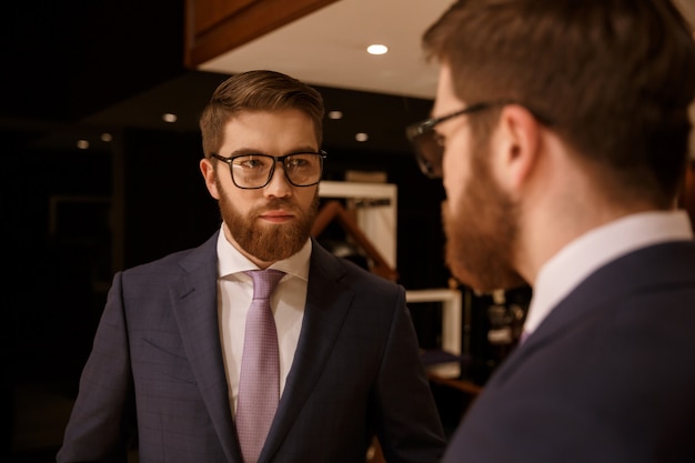 Free photo serious young bearded businessman looking at mirror