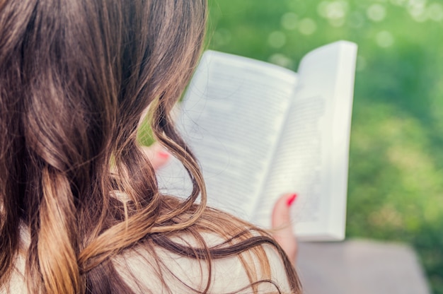 Free Photo serious young, beautiful girl holding an open book, read background summer green park. side view portrait of attractive young girl enjoying a good book sitting at sunny evening outdoors