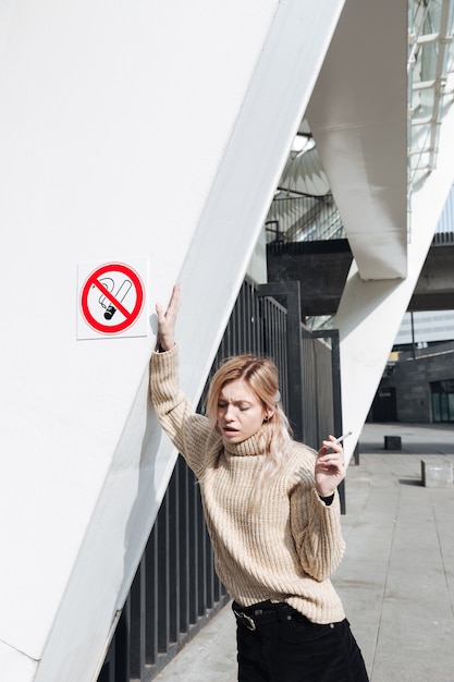 Serious young blonde lady with cigarette outdoors