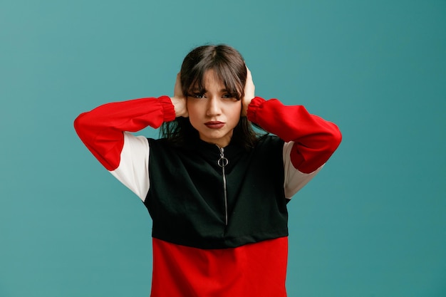 serious young caucasian woman looking at camera closing ears with hands isolated on blue background