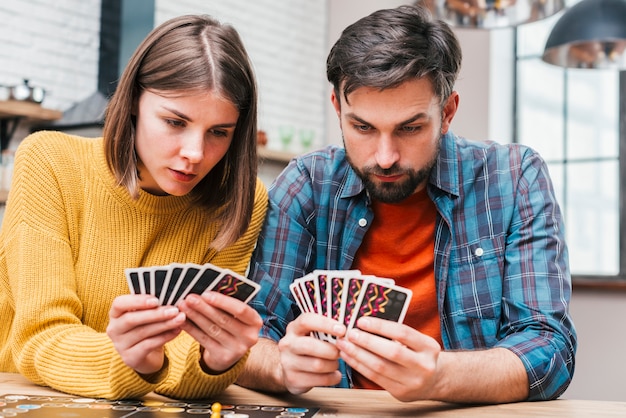 Free photo serious young couple looking at their cards playing the board game