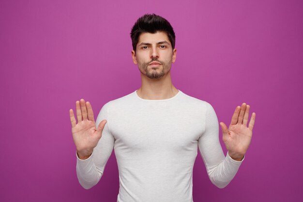 Serious young handsome man looking at camera showing empty hands on purple background