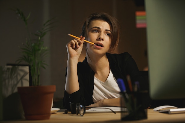 Serious young lady designer sitting in office at night