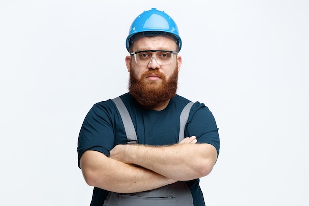 Free Photo serious young male construction worker wearing safety helmet uniform and safety glasses looking at camera with crossed arms isolated on white background