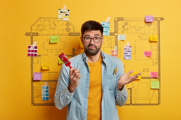 Free Photo serious young male stands next to house design sketch ready for renovation