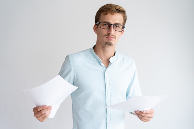 Free Photo serious young man holding paper sheets and looking at camera