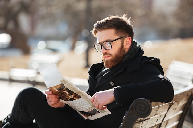 Serious young man sitting and reading newspaper in the city