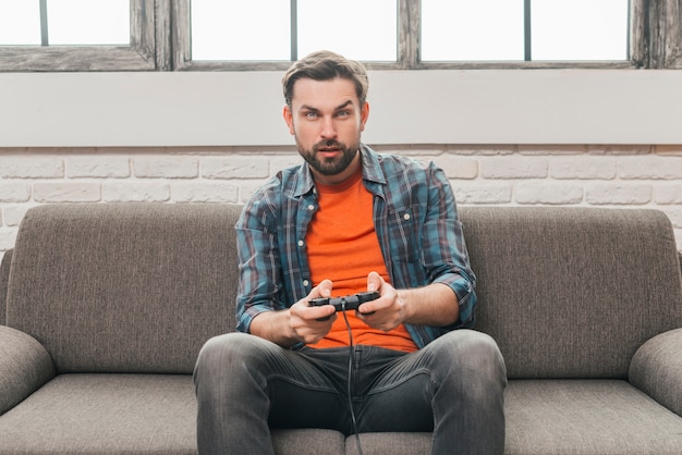 Serious young man sitting on sofa playing video game