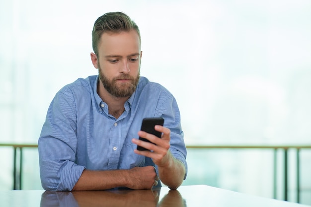 Serious Young Man Using Smartphone at Cafe Table