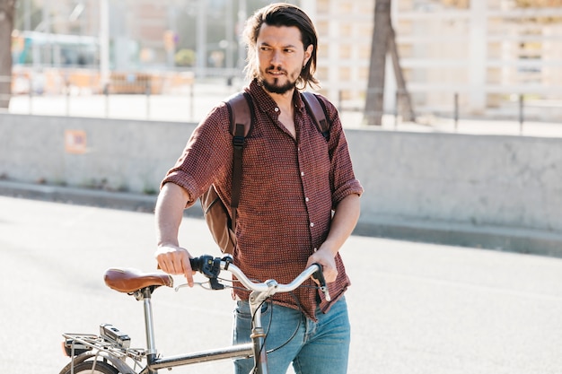 Free Photo serious young man with his backpack walking with bicycle