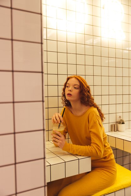 Serious young redhead curly lady sitting in cafe