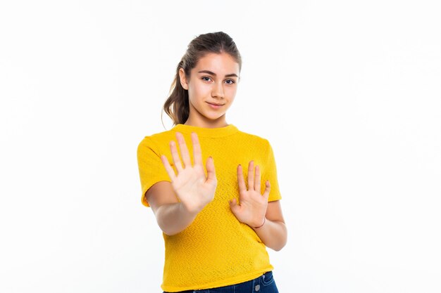 Serious young teen girl in casual making stop sign on white wall