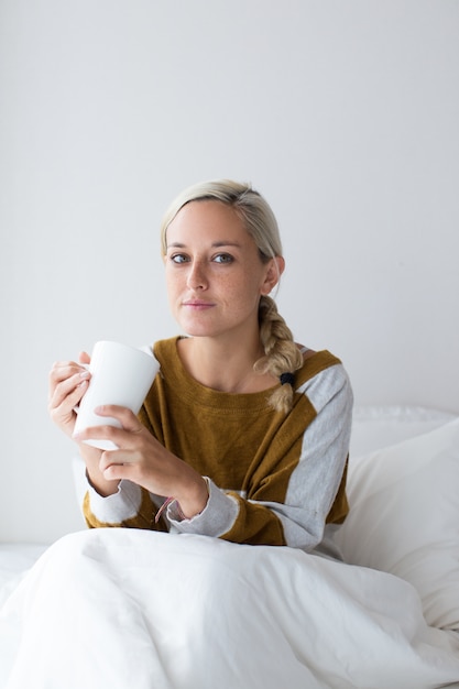 Free Photo serious young woman sitting on bed holding cup