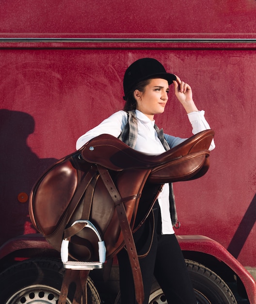 Free Photo serious young woman sitting outdoors and holding saddle