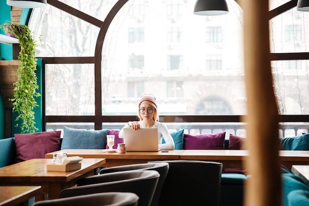 Free photo serious young woman sitting and using laptop in cafe