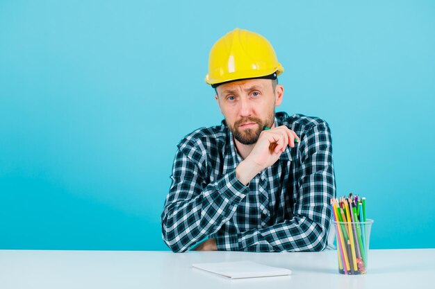 Seriously architect is looking at camera by sitting on blue background