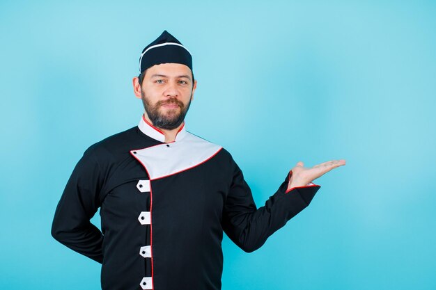 Seriously chef is pointing right with hand and putting other hand behind back on blue background