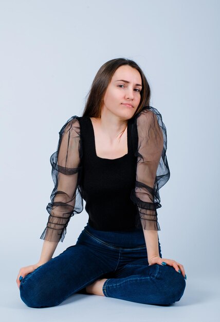 Seriously girl is looking at camera by sitting on floor on white background