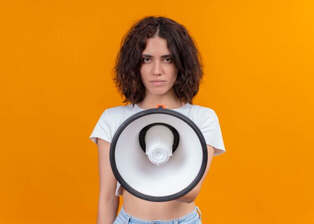 Seriously looking young beautiful woman holding speaker on isolated orange wall with copy space