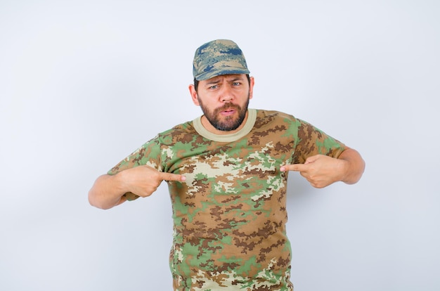 Free Photo seriously soldier is pointing himself with forefingers on white background