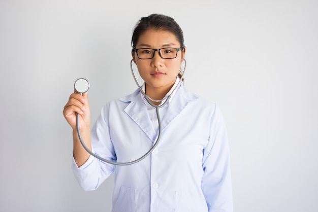 Serous young Asian female doctor using stethoscope. Medical testing concept.