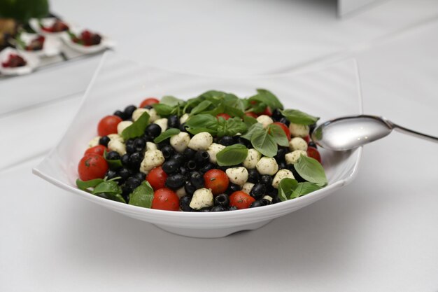 Serving of a delicious salad with cherry tomatoes, cheese, basil, anolives