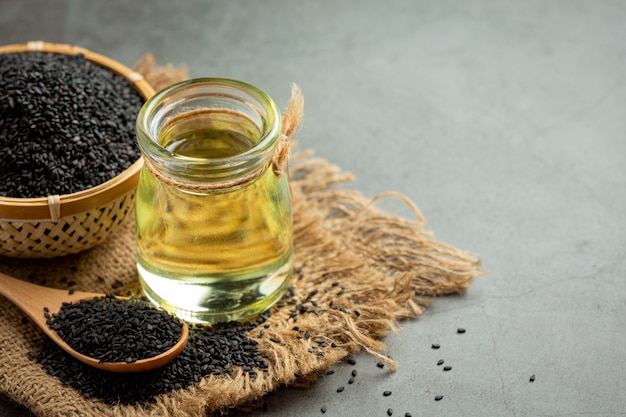 Sesame oil and raw black sesame seeds on dark background