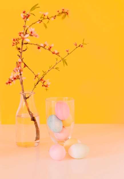 Set of bright Easter eggs near flower twig in vase with water