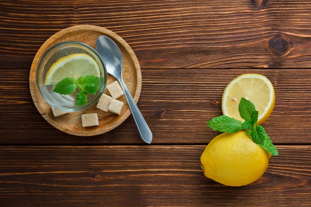 Free photo set of brown sugar and lemon slice in wooden plate and lemon and leaves on a wooden table