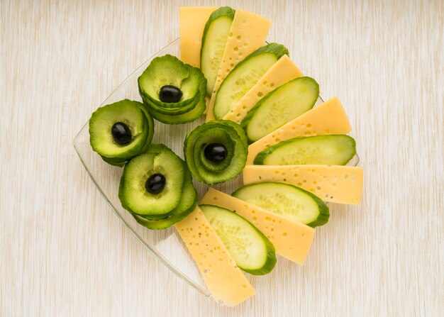 Set of cheese, cucumber and avocado with olives on plate