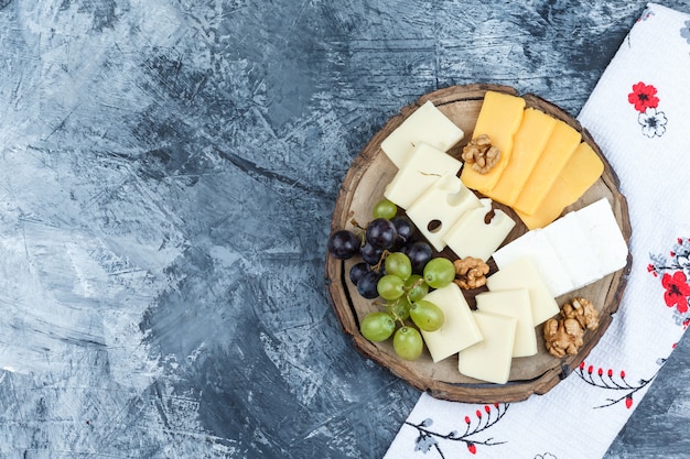 Free photo set of cheese, walnuts, kitchen towel and grapes on plaster and wood piece background. flat lay.