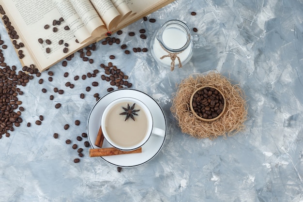 Set of coffee beans, book, milk, spices and coffee in a cup on a grey plaster background. top view.