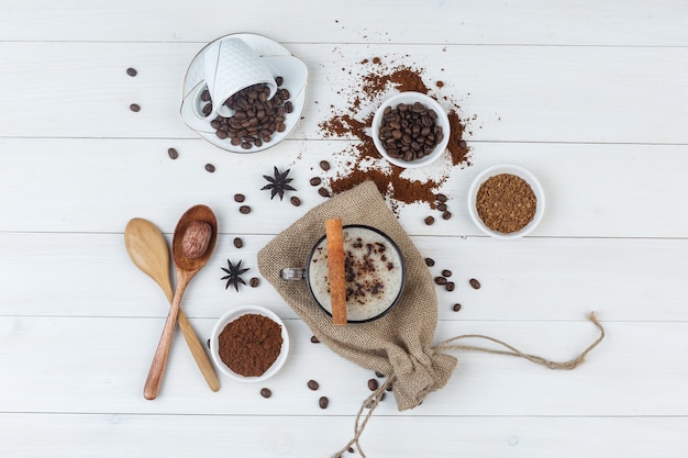 Set of coffee beans, grinded coffee, spices, wooden spoons and coffee in a cup on wooden and sack background. top view.