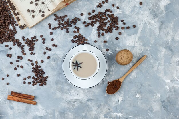 Set of cookies, coffee beans, grinded coffee, book, spices and coffee in a cup on a grey plaster background. top view.